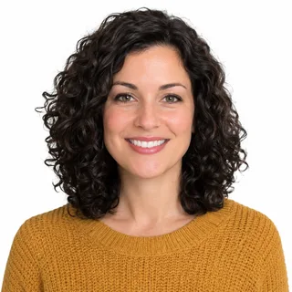 Curly-haired woman in a mustard sweater smiling at the camera, chest up