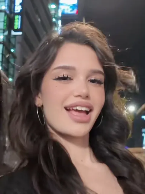 The friend in the middle of the group selfie, dark wavy hair and hoop earrings